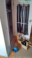 Belts hanging on wall-mounted rack along with belt hangers, wooden shoe rack on floor with wooden crate of brushes and Ronson tool.