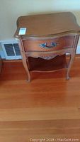 Side view of the wooden side table showing drawer with metal handle, curved legs, and lower shelf