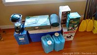 Overall view of lot with stove, cooler, lanterns, water jugs, sleeping bag and paddles