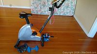 Full side view of silver and orange Tempo Fitness exercise bike with black seat and pedals on wooden floor