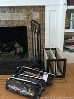 Fireplace tool set next to log holder and three packages of fire logs on wooden floor.