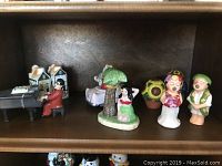 Ceramic salt and pepper shakers including houses, piano player, mermaid, and floral-themed characters arranged on a shelf