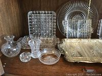 Wide shot showing a variety of clear crystal and glass serving pieces including vase, small bowls, rectangular and square serving dishes with various cut patterns.