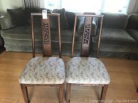 Two matching wooden chairs placed side by side showing full view with carved backrests and upholstered seats.
