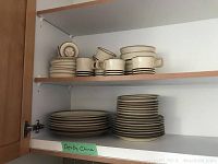 Assortment of stacked plates, bowls, cups and saucers arranged inside cabinet