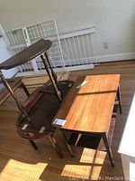 Three wooden tables stacked and arranged in a room with hardwood flooring, showing size and style differences among them.
