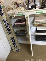 Overall view of fabric shelves with various folded fabrics and a large roll of fabric leaning against the wall.