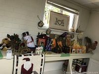 Overview of various holiday decor laid on a white table beneath a window, including tins, wreaths, figurines and wall hangings.