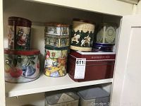 Photo of various Christmas-themed decorative tins including round tins with Santa Claus, ornaments, gnomes, and carousel horses, plus a large red rectangular Hudson's Bay tin.
