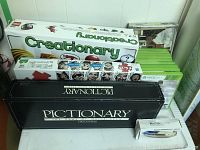 Stack of board games and Xbox 360 game cases including Pictionary, Creationary, Life, and Xbox games plus a candle box.