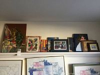 Full view of multiple framed art prints and needlepoint artwork arranged on a shelf.