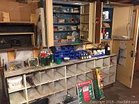 Overview of cubby storage, plastic bins with small hardware and fasteners, hand plane, bucket of Fast Patch compound, and metal cabinet with open doors full of hardware items.