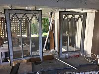 Two matching vintage wood framed windows hanging indoors with visible geometric muntins and glass panels.