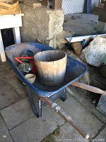 Front and top view of the blue metal wheelbarrow showing its contents including a wooden bucket and small containers.