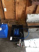Overview of black storage crate with coiled blue air hose, air ratchet wrench, and air spray gun on concrete floor