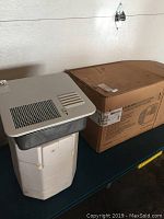 Photo of water heater unit next to its box showing packaging and heater details.