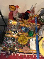 Photo showing colorful glass rooster and pelican figurines, clear crystal animals, and other glass pieces on patterned cloth