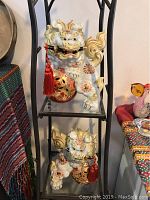 Two ceramic and gold painted Foo Dogs displayed on black metal shelving, showing overall appearance and scale.
