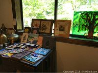 Photo of various decorative tiles and framed tile art on a wooden surface by a window.
