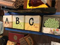 Photo showing all three Rae Dunn ceramic alphabet blocks A, B, C arranged next to green Threshold handmade ceramic flower with packaging and background items.
