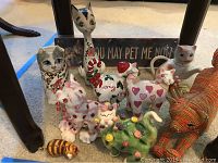 Full view of the ceramic and beaded cat figurine collection arranged beneath a table, showing all items and a pet-related sign in background.