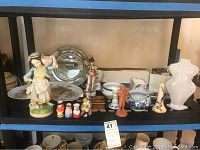 Shelf with multiple ceramic figurines, nested dolls, plates and decorative objects.