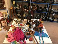 Wide angle view of the wooden puppets, masks, toys and figurines spread across a table including marionettes, carved masks, and dragon figurine.