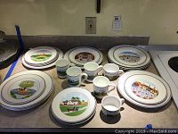 Overview of stacked dinner plates, side plates, coffee mugs, and tea cups with scenic prints.