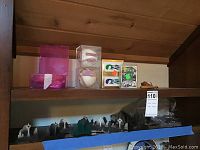 View of two signed baseballs in clear display cases, pink boxes, trivia cards, and other items on upper shelf with metal skyline napkin holders visible on lower shelf.
