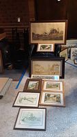 View of all framed prints and original oil painting arranged on floor showing their various sizes and subjects including historic ships and buildings.