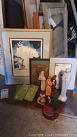 Photo showing three framed prints leaning against a surface alongside various figurines including knitted and ceramic types.