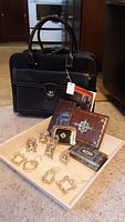 Black Samsonite tote bag shown with leather wallets and the ornamental box on carpeted floor, illustrating the main items of the lot.