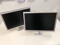 Two Apple monitors shown from front, silver aluminum bezel with black screens, likely 22-inch and 24-inch models.