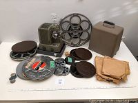 Wide view of the vintage film projector surrounded by film reels, canisters, and cases, showing the full content of the lot.