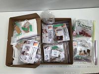 Overview photo showing multiple boxed and bagged all wood dollhouse furniture kits in original packaging, sorted in cardboard box.