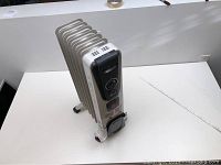Full view of off-white portable radiator heater standing on caster wheels on a white table.