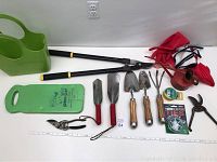 Photo of the entire garden lot showing all gardening tools, gloves, watering can, kneeling pad, and twist ties laid out on a white surface.