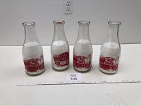 Four vintage Calnans Dairy glass milk bottles with red logo and filled with white styrofoam beads, displayed on white surface with ruler for scale.