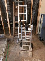Photo showing the wooden ladder, aluminum ladder leaned against the wall, and the folded Cosco aluminum hand trolley on the floor.