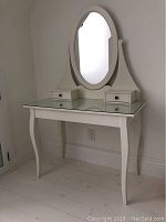 Front view of white IKEA Hemnes vanity table with attached oval mirror and two small drawers, showing full table and mirror.