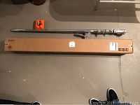 Top-down view showing two chrome boom arm tubes, original cardboard box, and orange counterweight block laid out on the floor.