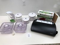 Full lot layout showing FoodSaver vacuum sealer, sealed containers, rolls of vacuum bags, and additional storage containers.