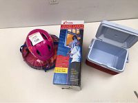 Photo showing pink Giro bike helmet on top of pink and orange SwimWays inflatable baby floater in plastic bag, Kidde escape ladder box, and a small red and gray cooler with hinged lid.