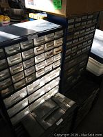 Photo of three metal hardware organizers with many small clear drawers, some labeled, in blue and black finish.