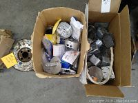 Two cardboard boxes filled with various metal electrical components such as junction boxes, switch boxes, wire, and seals.