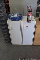 Two white single door metal cabinets with extra shelves, placed side by side, with the air hose and Swivel Sweeper box on top.