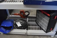 Shelf showing orange electric hedge trimmer, black Econo Line tool balancer, and black plastic storage container with small drawers