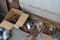 Wide shot of three boxes containing various copper plumbing fittings and pipes, placed on the ground near a corrugated metal wall.