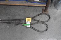 Two thick steel wire rope slings with looped ends lying side by side on concrete floor with a yellow tag indicating size: 3/4 by 10 ft.
