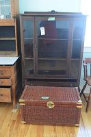 Front view of china cabinet with closed glass doors and wicker chest positioned in front